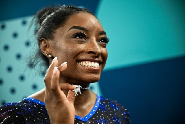 Simone Biles poses with her goat necklace after winning the women's gymnastics all-around