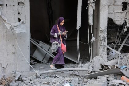 A woman checks her phone amid the rubble of a building destroyed by Israeli bombardment in