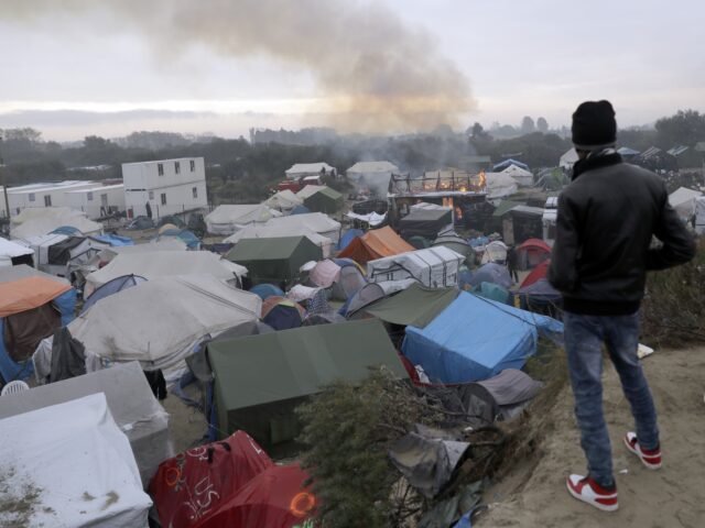 A migrant watches burning shelters set on fire in the makeshift migrant camp known as &quo