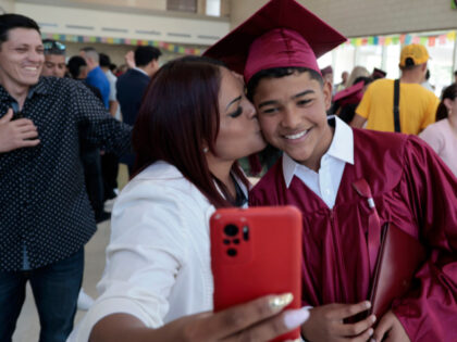 Venezuelan migrant and graduate Adrian Davila gets a kiss and takes a selfie with his moth