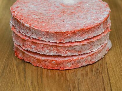 Frozen beef burger patties are placed on a wooden cutting board before cooking.