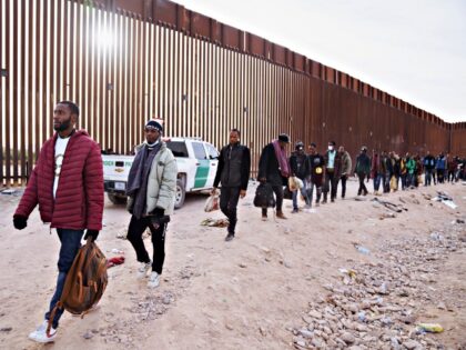 Migrants walk beside the US-Mexico border fence in Lukeville, Arizona, US, on Monday, Dec.