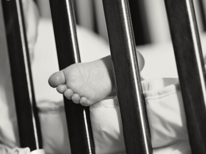 A child's foot sticking through the bars of a cot - stock photo