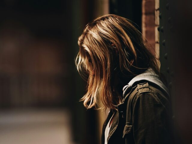 woman leaning against a wall in dim hallway