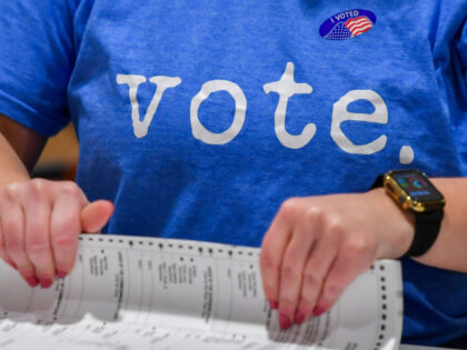 A woman wearing a Vote t-shirt prepares mail-in ballots to...