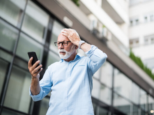 Shocked man is looking at his phone and has his hand on his head.