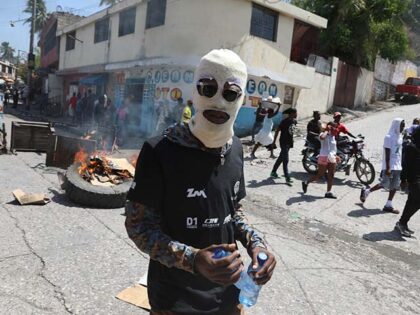 A masked demonstrator walks past a burning roadblock placed by protesters demanding that t