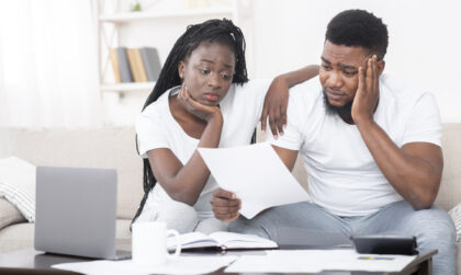 Debt concept. Portrait of sad afro couple looking at invoice, upset about huge bills, not