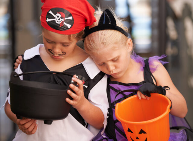 A brother and sister sulk together and look at their empty sweet baskets on halloween