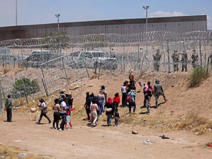 Migrants attempting to enter the United States through a barbed wire fence installed along