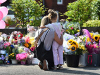 A mother hugs her child as they look at floral tributes for the victims of a deadly knife