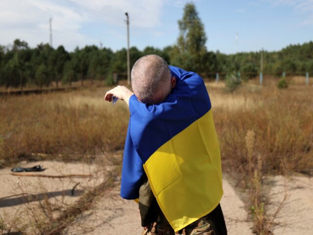 TOPSHOT - A Ukrainian serviceman wrapped in a Ukrainian flag reacts after being released f