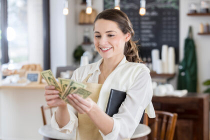 Cheerful young female Hispanic waitress smiles while counting out a large tip.