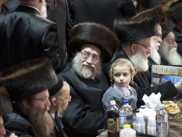 A young boy sits with a group of elderly men listen as members of the Satmar Hasidic commu