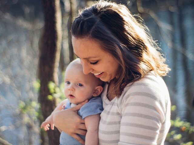 woman carrying baby near trees