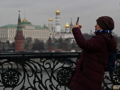 A woman takes pictures with a smartphone standing on the pedestrian Patriarchal Bridge ove