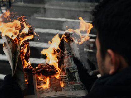 man holds burning newspaper