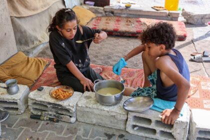 Displaced children eat a cooked meal in their tent at Gaza City's damaged Yarmouk stadium