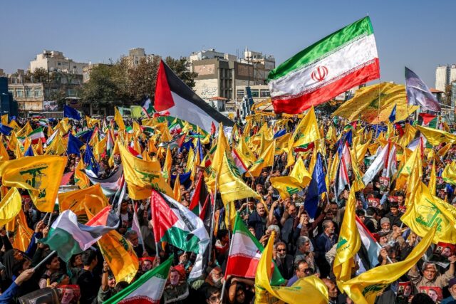 Mourners in Mashhad, Iran, wave flags of Iran, Palestine, and Hezbollah during a funeral p