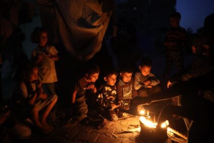 Palestinian children sitting around a fire in the rubble of Gaza