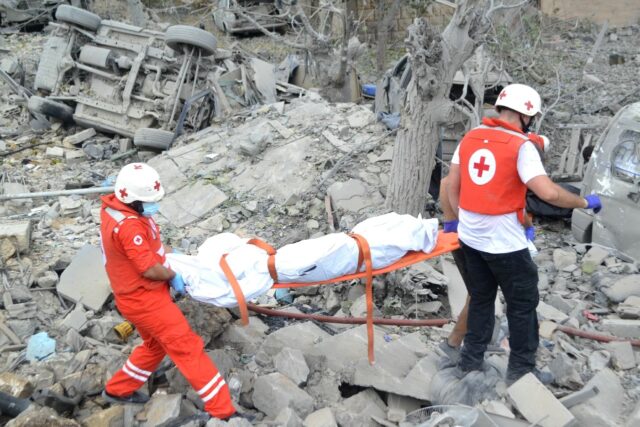 Paramedics carry a body from the rubble at the site of the Israeli airstrike in Aito