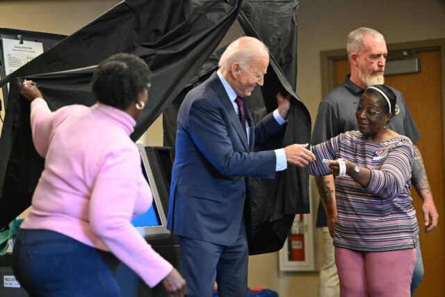 US President Joe Biden is handed an 'I Voted' sticker as he steps out of the booth after c