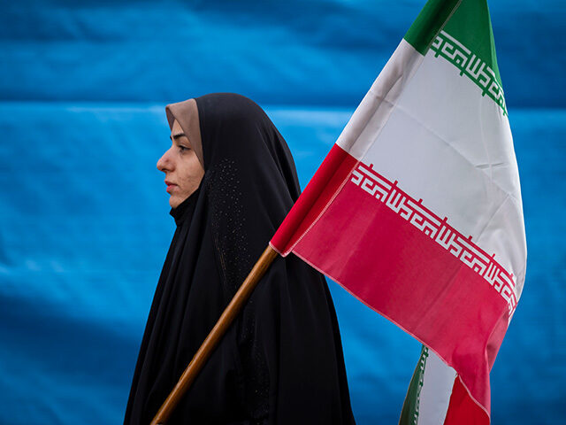 A veiled Iranian woman carrying an Iran flag while attending a gathering out of the former