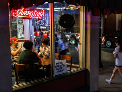 A group of three college boys wave a group of college girls walking past the restaurant lo