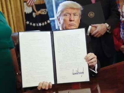 President Donald Trump holds up an executive order after his signing the order in the Oval