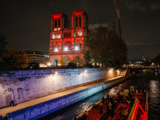 an open excursion boat (Bateau-Mouche) passing in front of the Notre-Dame cathedral illumi