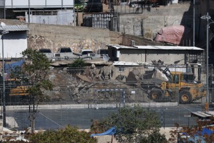 An excavator demolishes a home belonging to the Al-Ruwaidi family in Al-Bustan