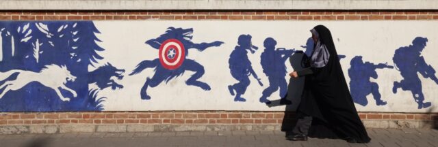 An Iranian woman walks past a mural on the side wall of the former US embassy in Tehran, t