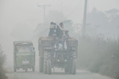 Commuters ride along a highway engulfed in smog, on the outskirts of Lahore