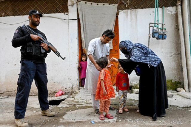 Elite police personnel standing guard as a health worker administers polio drops to a chil