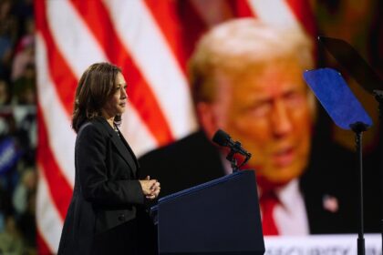 Before a large image of Donald Trump, Kamala Harris speaks at a campaign event in Erie, Pe