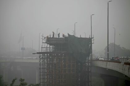 Labourers stand on a scaffolding amid dense smog in New Delhi on November 13, 2024