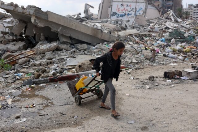 A Palestinian girl transports clean water past a destroyed building in Gaza City, in the t