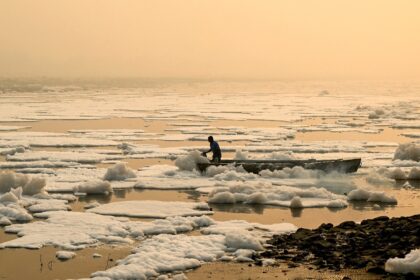 A man steers his boat across river Yamuna laden with toxic foam