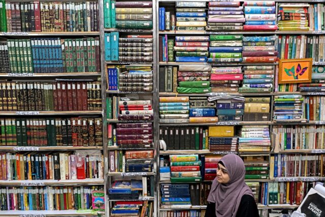 A student sits beneath packed shelves at the Hazrat Shah Waliullah public library