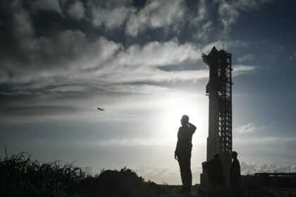 A man watches a SpaceX plane as it flies past the SpaceX Starship at the launch pad ahead