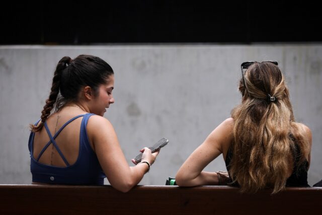 Two women sit on a bench looking at their phone in central Sydney. The Australian governme