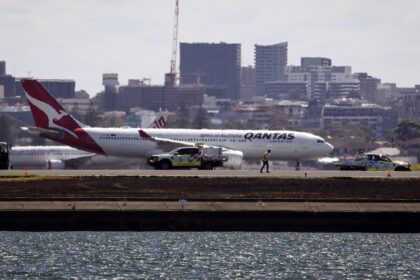 Workers check the runway as a Qantas plane prepares to take off behind them at Sydney Airp