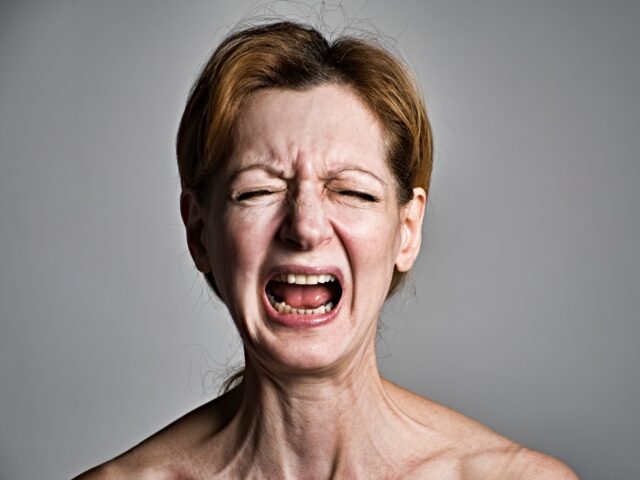 Head and shoulders studio portrait of a red-haired woman, screaming in an intense expressi