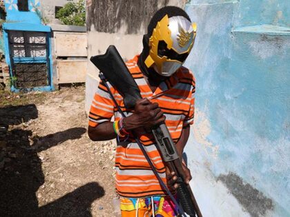 A masked, armed gang member poses for a photo at the National Cemetery during the Fete Ged