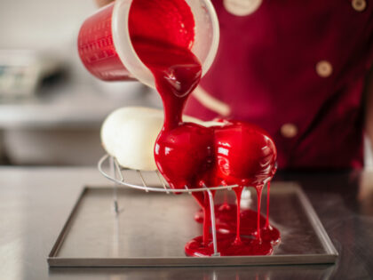 Mid adult woman decorating and pouring red syrup over red cakes in heart shape. She works