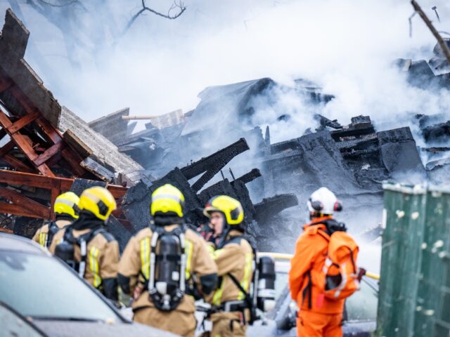 Firemen stand next to a partially collapsed residential building following a fire and an e