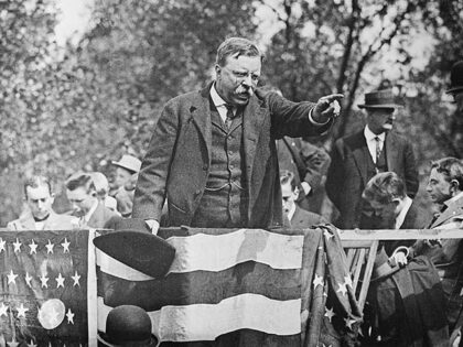 Theodore Roosevelt standing on a podium pointing into the crowd during a campaign rally sp