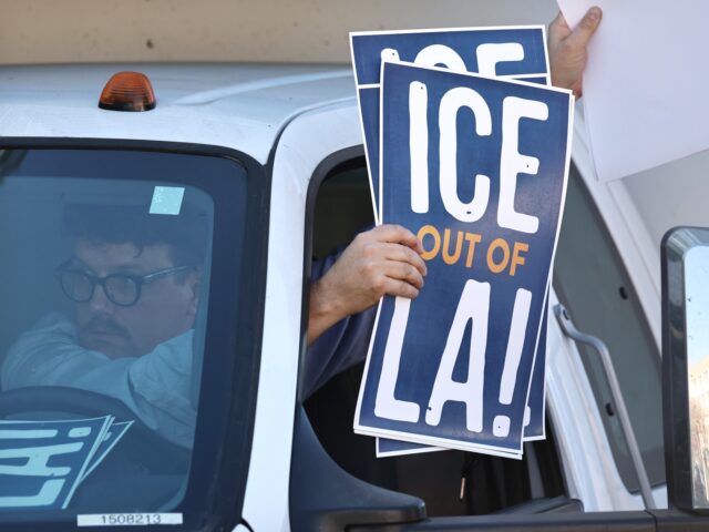 LOS ANGELES, CALIFORNIA - DECEMBER 18: A supporter waves "ICE Out of LA!' signs as immigra