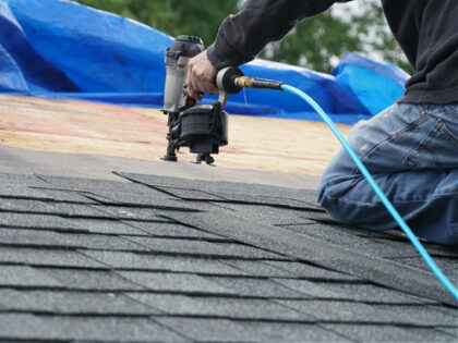 Handyman using nail gun to install shingle to repair roof - stock photo