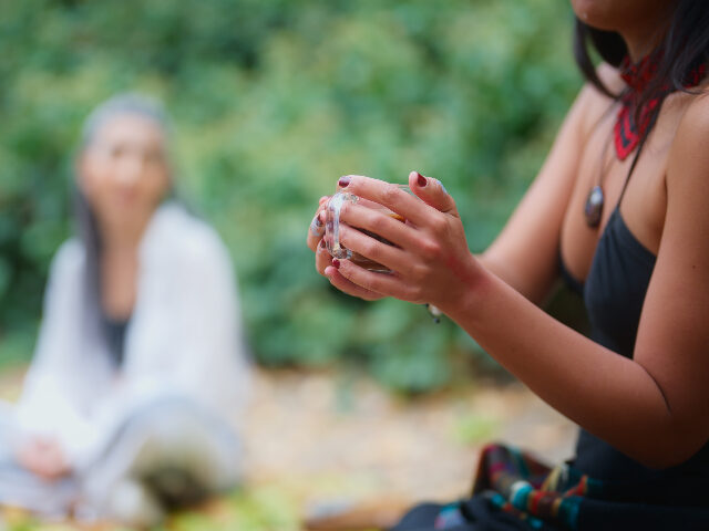 A woman in a black dress is serving cacao drinks during a cacao ceremony in nature. A caca